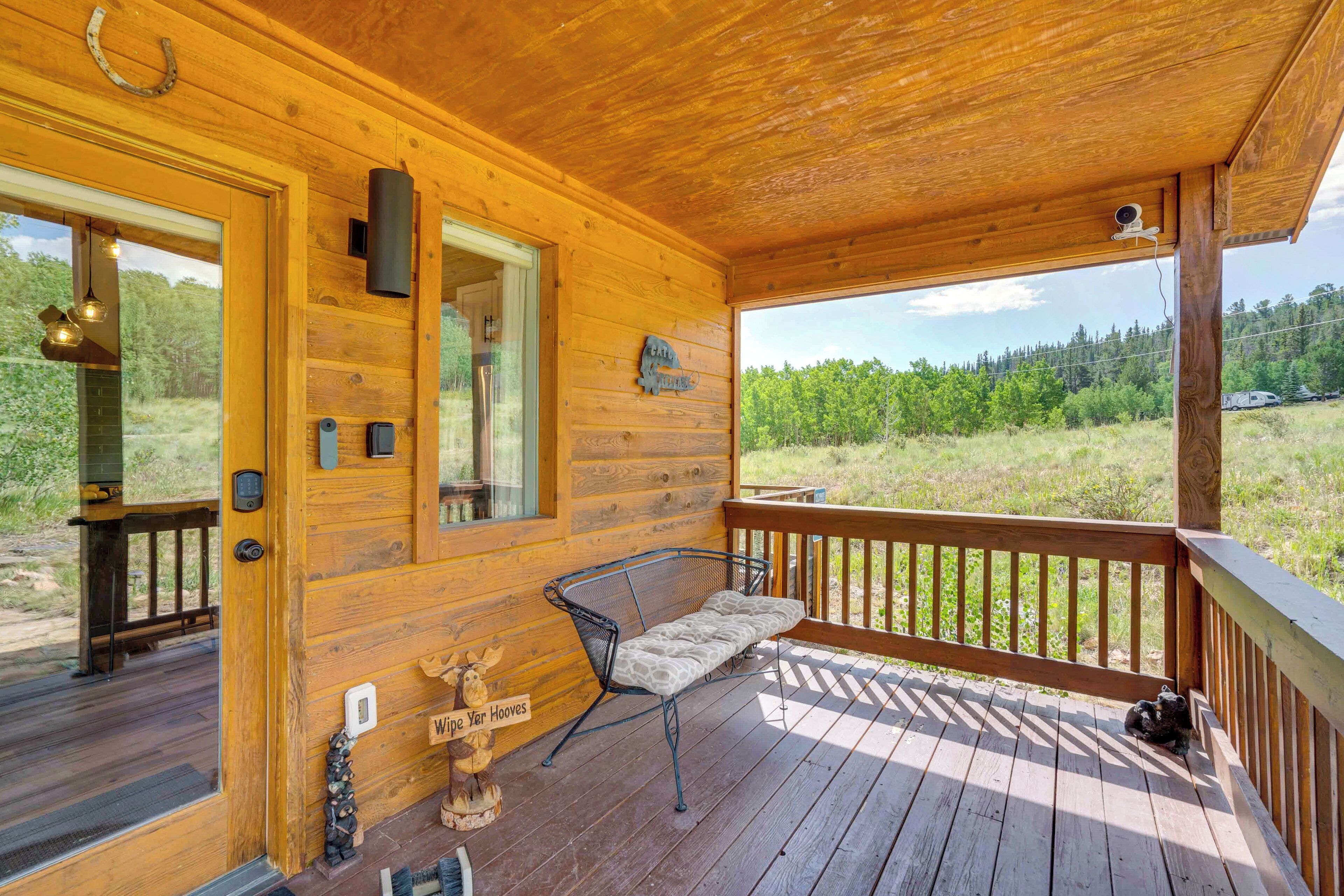 Une cabane en bois dotée d’une véranda, d’un banc et offrant une vue sur la forêt environnante.