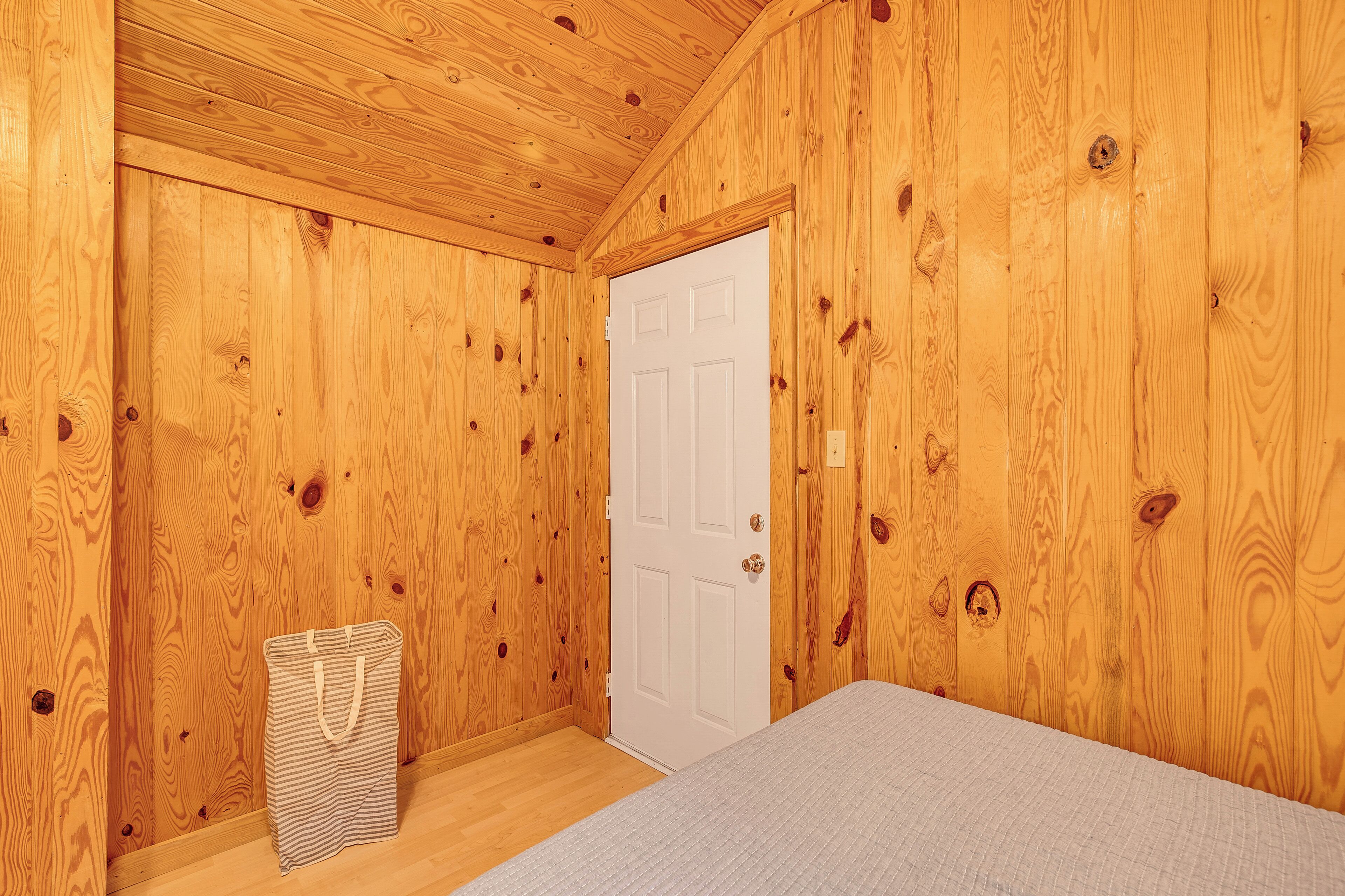 A wooden-paneled room with a bed, a white door, and a striped bag on the floor.