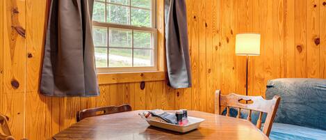 L’intérieur d’un chalet en bois, avec une table à manger, des chaises, un canapé et une fenêtre avec des rideaux.
