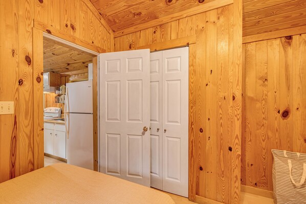 A wooden-paneled room with a bed, a white door, and a kitchen area visible through an open doorway. - Clarkson Cabin Near Nolin Lake: 4 Mi to Boat Ramp! (Clarkson)