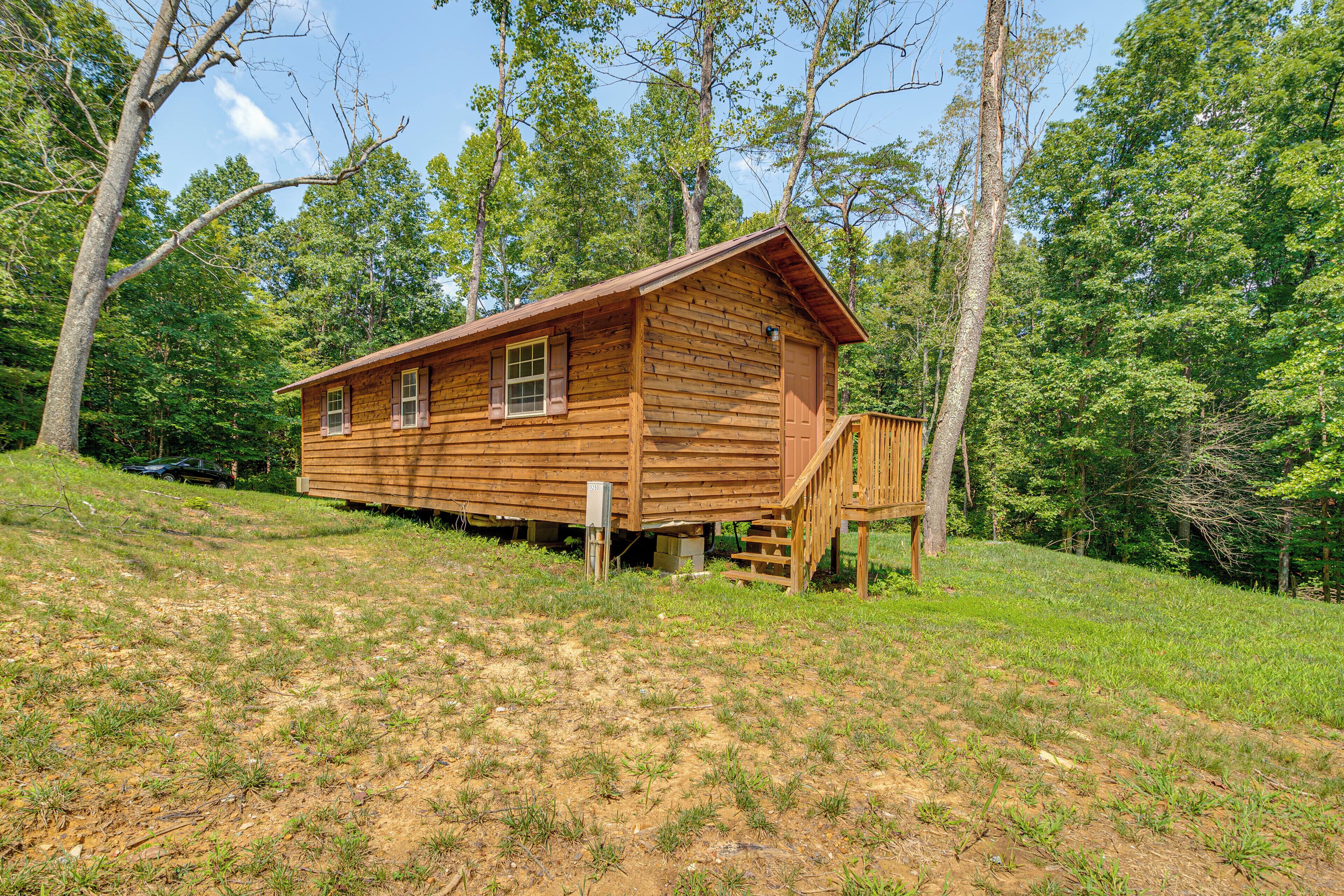 A wooden cabin with a front porch and a small deck, surrounded by trees.