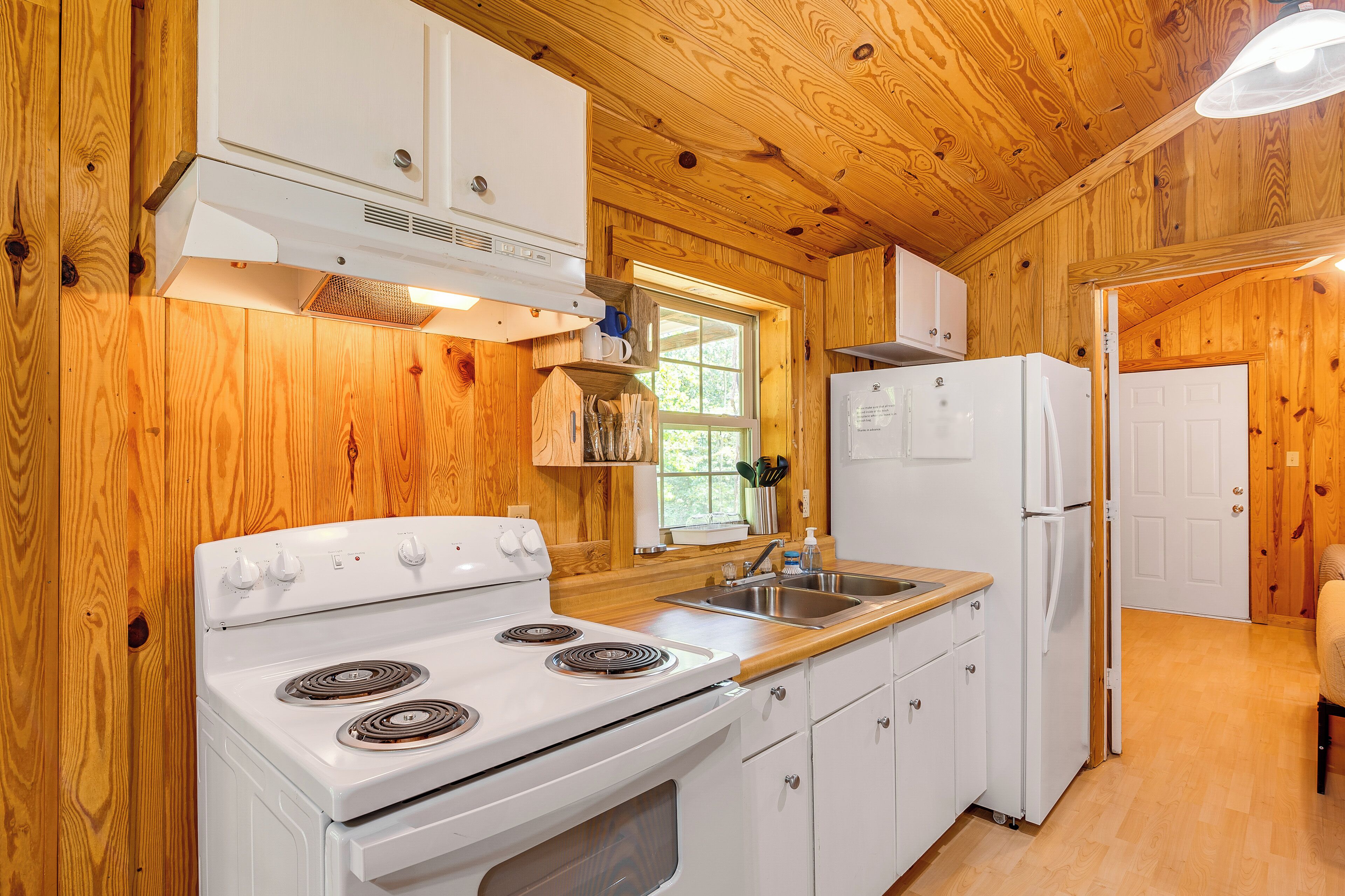 A wooden-paneled kitchen with white appliances, including a stove, sink, and refrigerator.
