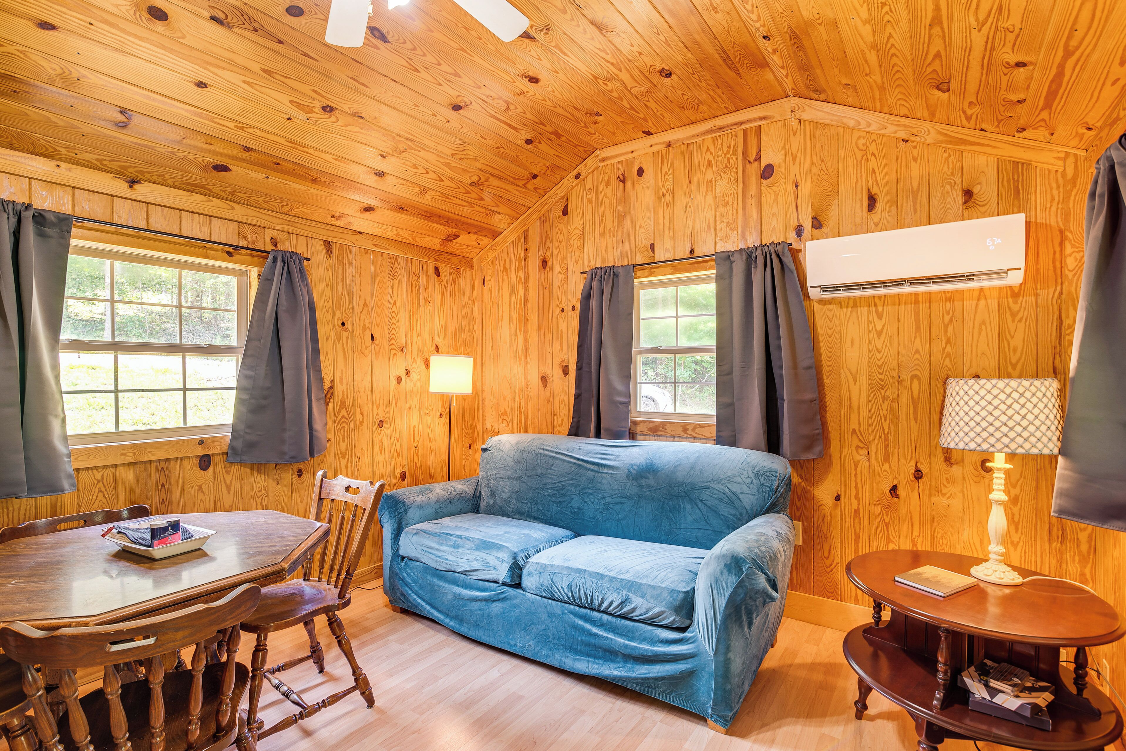 A wooden cabin interior with a sofa, dining table, chairs, and a lamp.