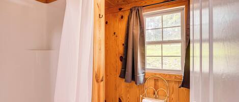 A wooden cabin bathroom with a shower, toilet, and a window.