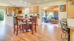 A spacious kitchen with wooden cabinets, a dining area with a table and chairs, and a view of the outdoors through large windows. - Mountain-view Maine Cabin: Ski, Hike & Bike! (Strong)