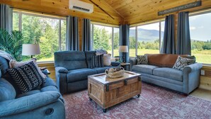 A cozy living room with two sofas, a wooden coffee table, and a view of mountains through large windows. - Mountain-view Maine Cabin: Ski, Hike & Bike! (Strong)