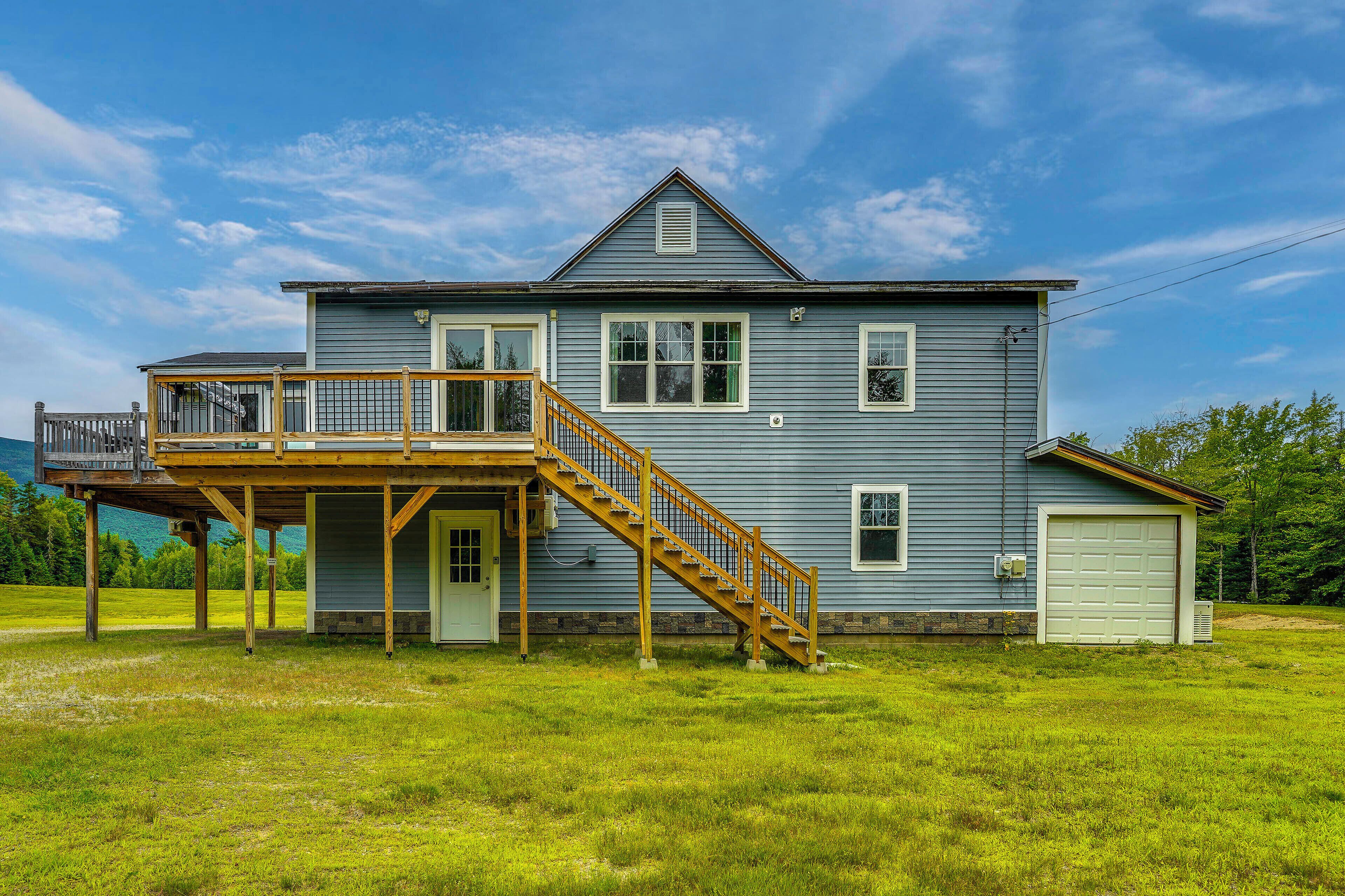 A two-story house with a wooden deck and a staircase leading to the second floor.