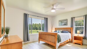 A bedroom with a wooden bed, a nightstand, a desk, and a large window with curtains. - Mountain-view Maine Cabin: Ski, Hike & Bike! (Strong)