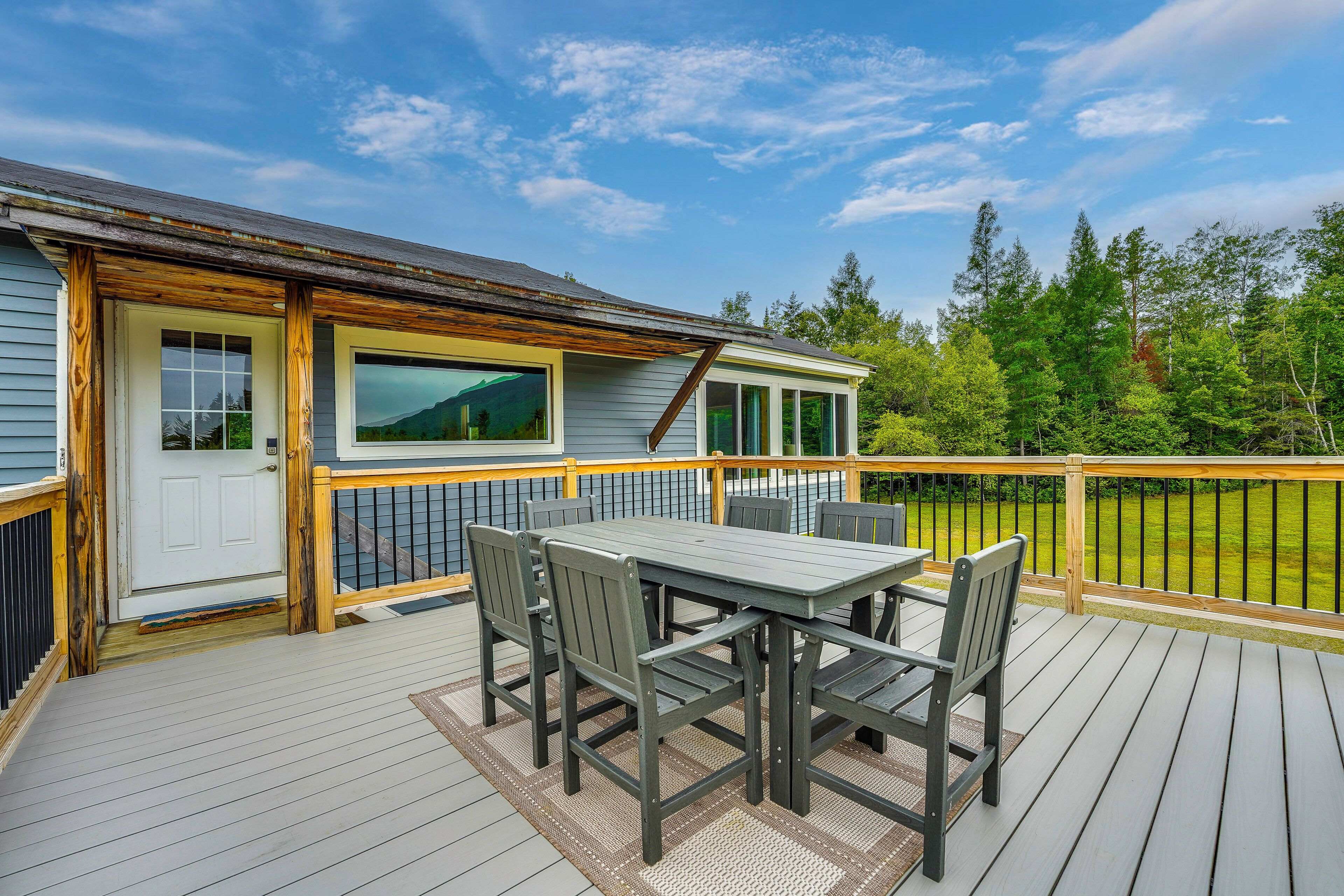 Une terrasse en bois avec une table et des chaises, un espace couvert avec une fenêtre, et une vue sur une forêt.