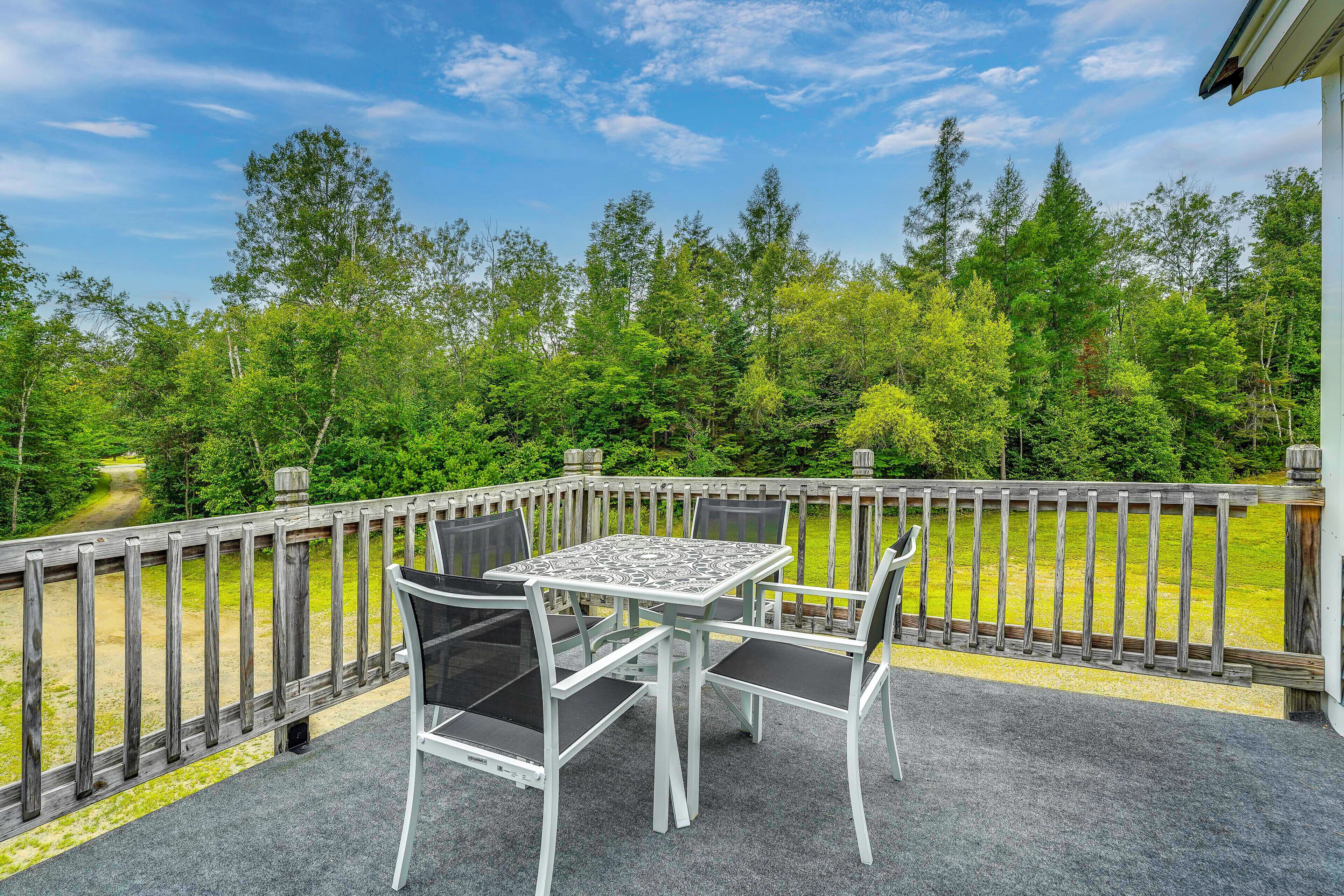 A patio with a table and chairs, surrounded by a wooden fence, overlooking a forested area.