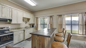 A kitchen with a central island, wooden chairs, a stove, and a view of a lake through large windows. - Quiet Lake Gladewater Getaway w/ Dock & Kayaks! (Gladewater)