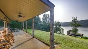 A covered outdoor area with wooden rocking chairs, a concrete floor, and a view of a lake and hills. - Quiet Lake Gladewater Getaway w/ Dock & Kayaks! (Gladewater)