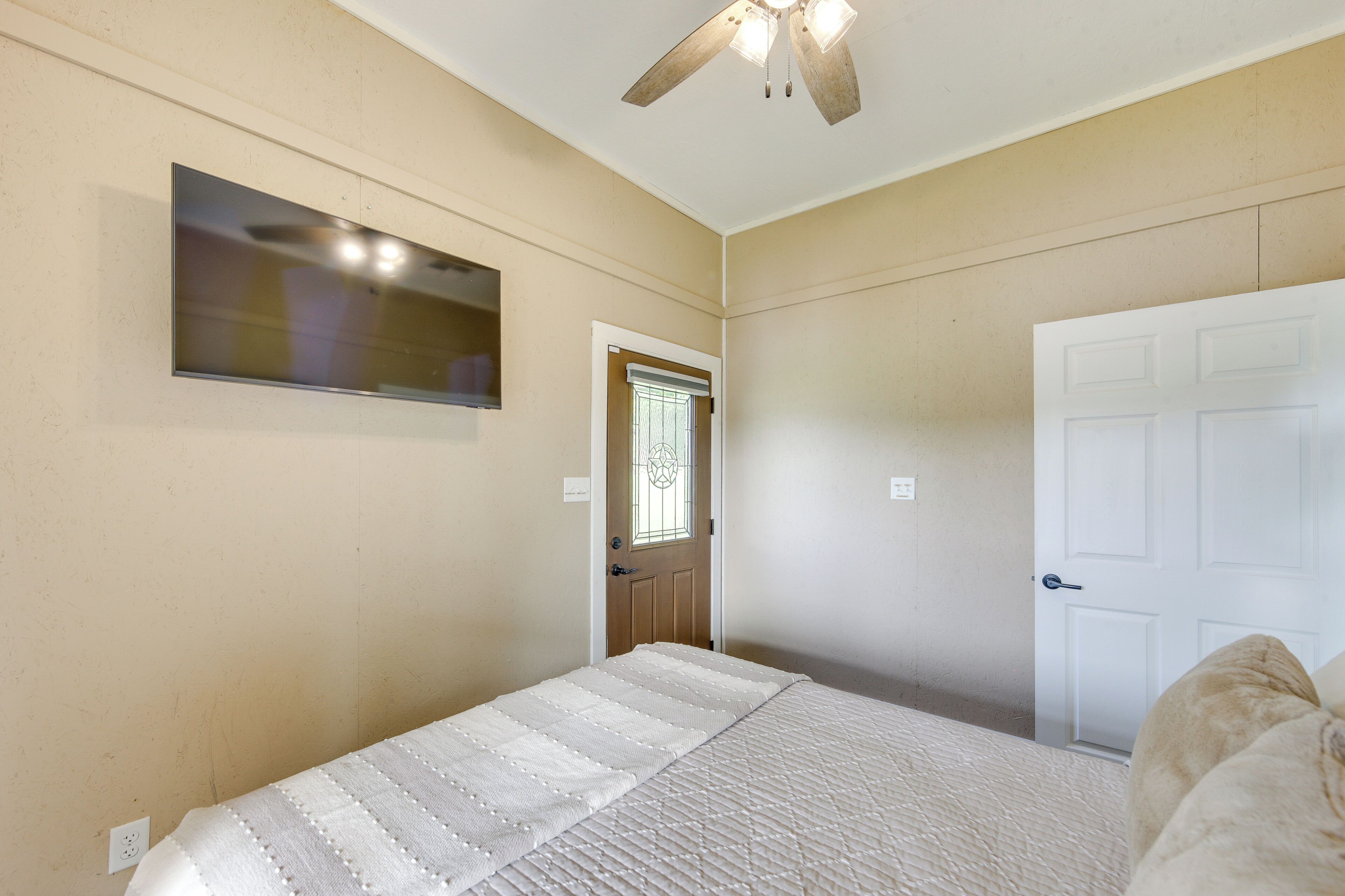 A bedroom with a bed, a ceiling fan, a door, and a window.