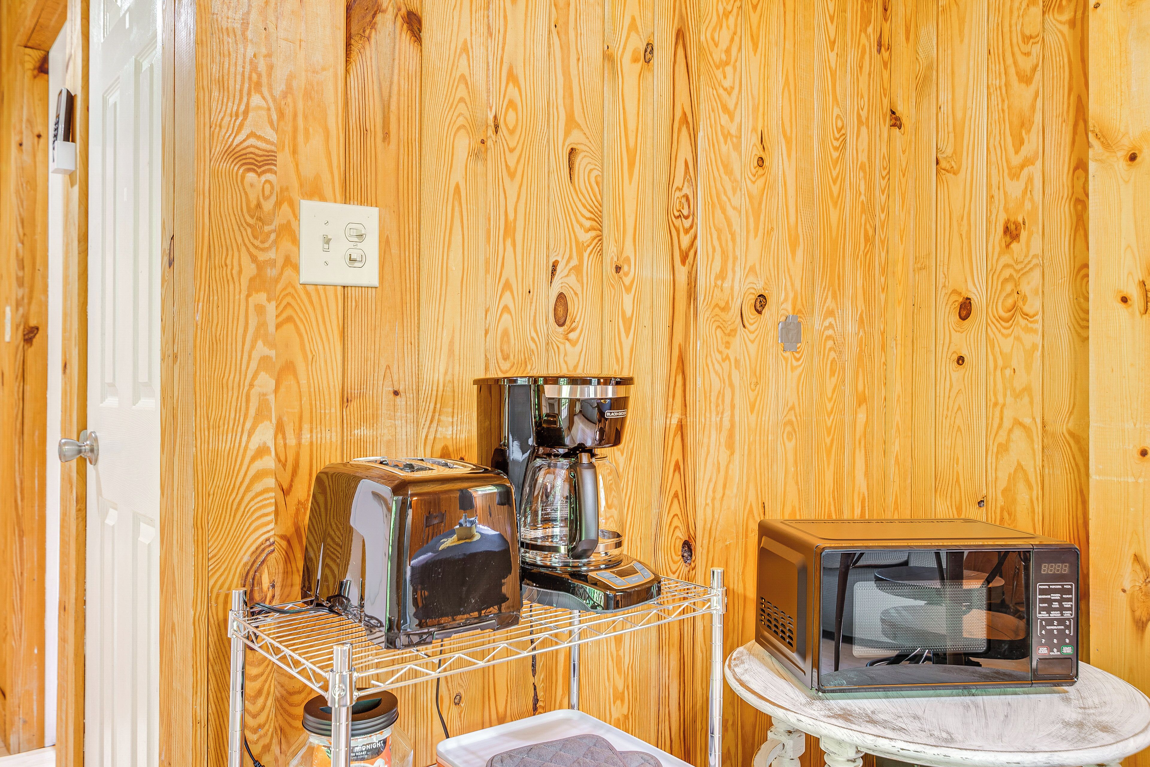Una cocina con paredes de madera, una cafetera, un tostador y un microondas sobre una pequeña mesa.
