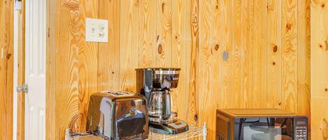 Una cocina con paredes de madera, una cafetera, un tostador y un microondas sobre una pequeña mesa.