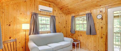 Una habitación de cabaña de madera con sofá, una mesita, una silla y una cama.