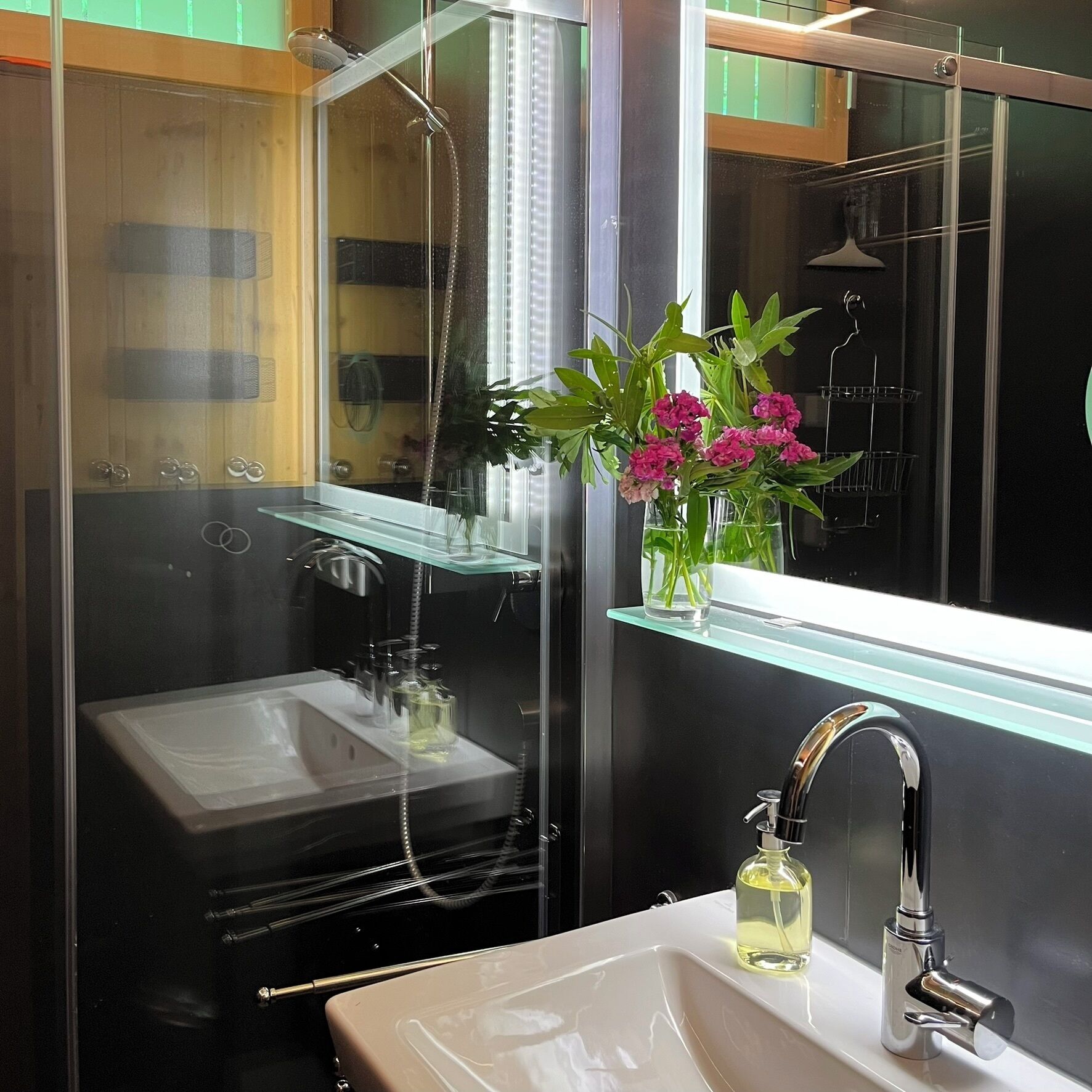 Ein modernes Badezimmer mit Duschkabine aus Glas, einem weißen Waschbecken und einem Spiegel darüber.