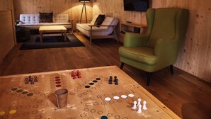 A cozy living room with a wooden floor, a green armchair, a sofa, a coffee table, and a board game. - Chalet Ablon (Saalbach-Hinterglemm)