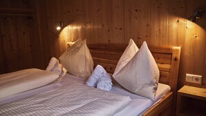 A wooden cabin-style room with two beds, each with white linens and pillows, and a small wooden nightstand with a lamp. - Chalet Ablon (Saalbach-Hinterglemm)