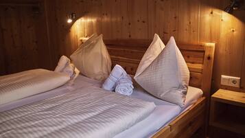 Ein holzgetäfeltes Zimmer im Blockhausstil mit zwei Betten, jeweils mit weißen Bettwäsche und Kissen, und einem kleinen Nachttisch mit einer Lampe.