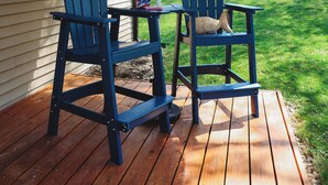 Una terraza de madera con dos sillas Adirondack bajo un paraguas a rayas.