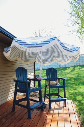 A wooden deck with two Adirondack chairs under a striped umbrella.