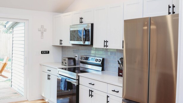 Una cocina moderna con gabinetes blancos, electrodomésticos de acero inoxidable y piso de madera.
