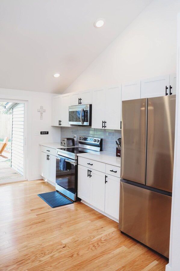 A modern kitchen with white cabinets, stainless steel appliances, and a wooden floor.