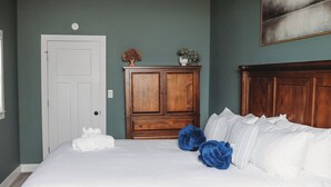 Un dormitorio con cama de madera, una puerta blanca, un armario de madera y un cuadro en la pared.