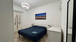Ett sovrum med en säng, ett skrivbord och ett nattduksbord. Det finns en tavla på väggen och en taklampa.