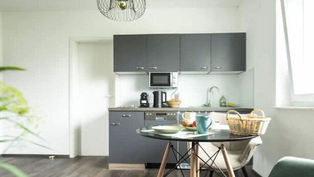 Una cocina moderna con armarios grises, un microondas y una cafetera. Hay una mesa redonda con una taza azul y una cesta.