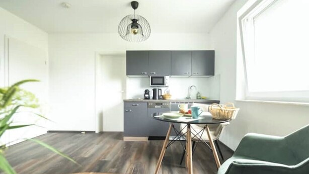 Une cuisine moderne avec des meubles gris, un four à micro-ondes et un coin repas comprenant une table et des chaises.