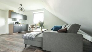 Un espacio tipo loft con sofá gris, una mesa de comedor y una zona de cocina.