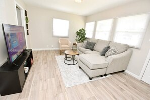 Un salon comprenant un canapé, une table basse, un téléviseur posé sur un meuble, un fauteuil et une plante.