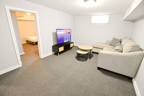 Un salon comprenant un canapé, une table basse, un téléviseur posé sur un meuble et une porte donnant sur une autre pièce.
