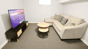 A living room with a flat-screen TV, a beige sofa, two round wooden tables, and a carpeted floor. - 5 min walk to Notre Dame! Modern home (517) (South Bend)