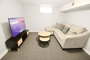 A living room with a flat-screen TV, a beige sofa, two round wooden tables, and a carpeted floor. - 5 min walk to Notre Dame! Modern home (517) (South Bend)