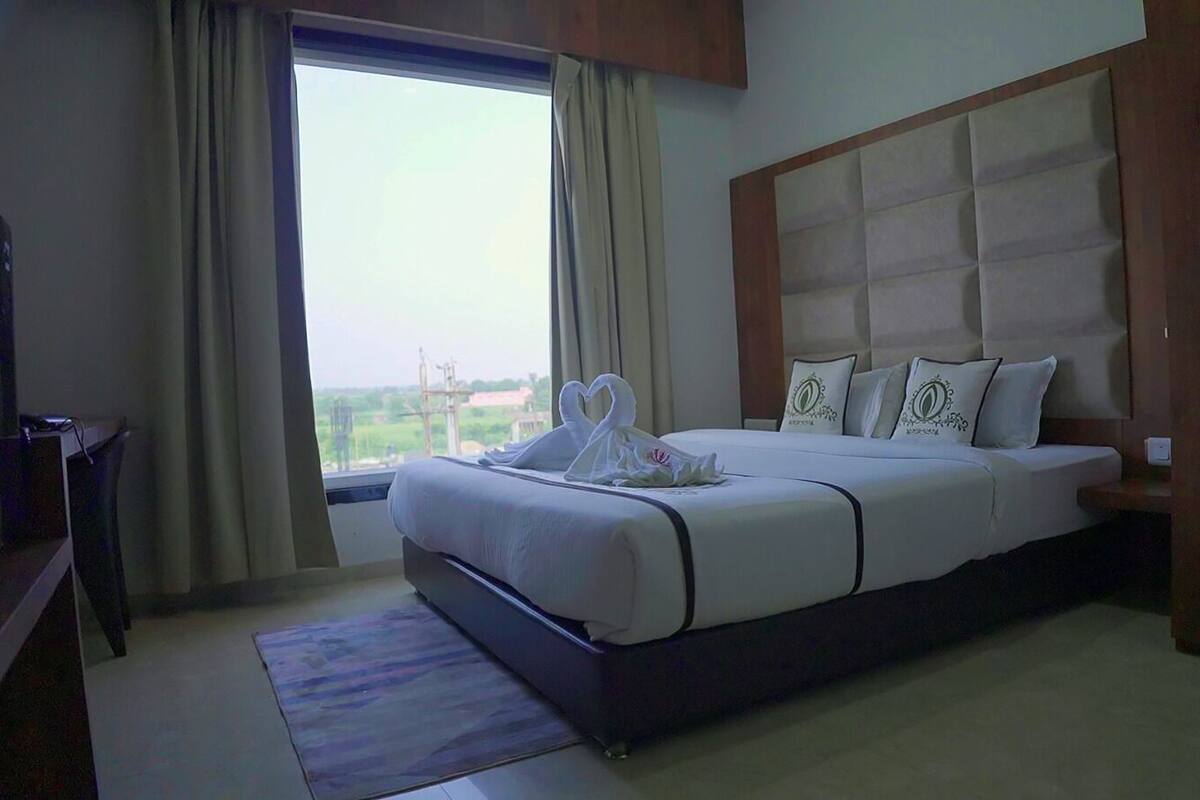 Habitación de hotel con una cama grande, cabecera de madera y vistas al exterior por la ventana.