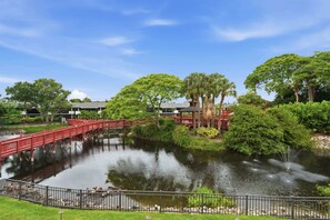 A serene lakeside view with a red bridge, lush greenery, and a clear sky.