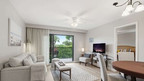 A living room with a sofa, a coffee table, a TV, and a dining area with chairs and a table. - F-236 - Deluxe Condo With Resort Views & Sleeps 6 (Naples)