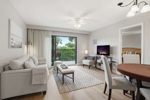 A living room with a sofa, a coffee table, a TV, and a dining area with chairs and a table.