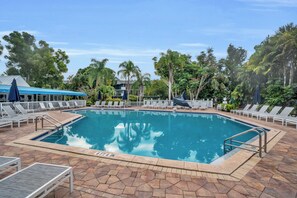 A rectangular swimming pool with a clear blue water surface, surrounded by a tiled deck with lounge chairs and umbrellas.