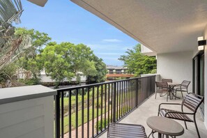 A balcony with a table and chairs, a railing, and a view of a tree and buildings. - I-253 - End Unit with Resort Views From Lanai (Naples)