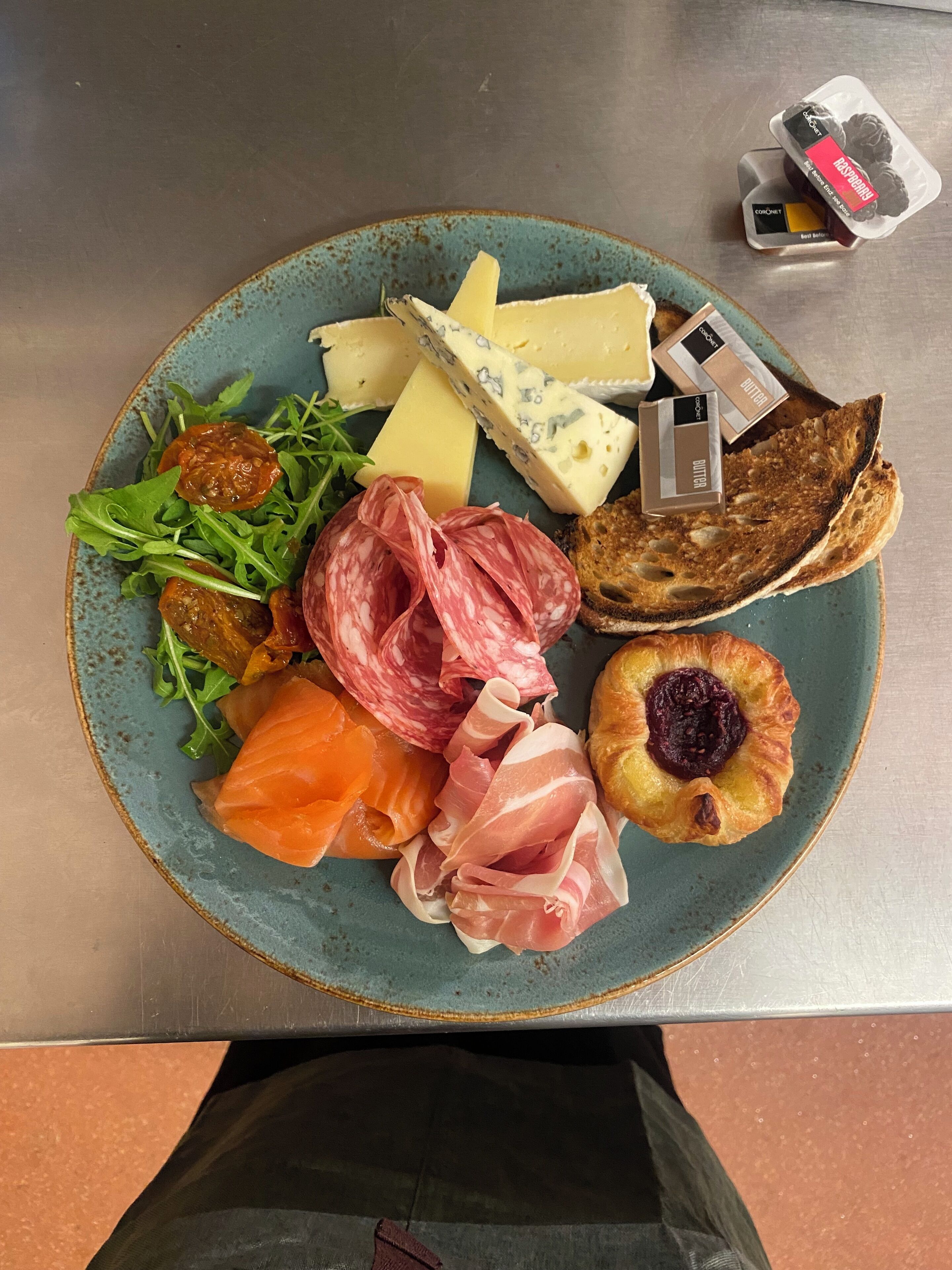 A plate with various cheeses, cured meats, and a pastry on a ceramic plate.
