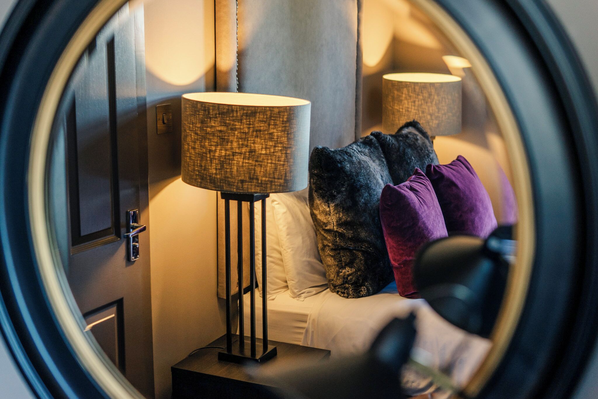 Un dormitorio con cama, mesita de noche, lámpara y ventana con vistas al exterior.