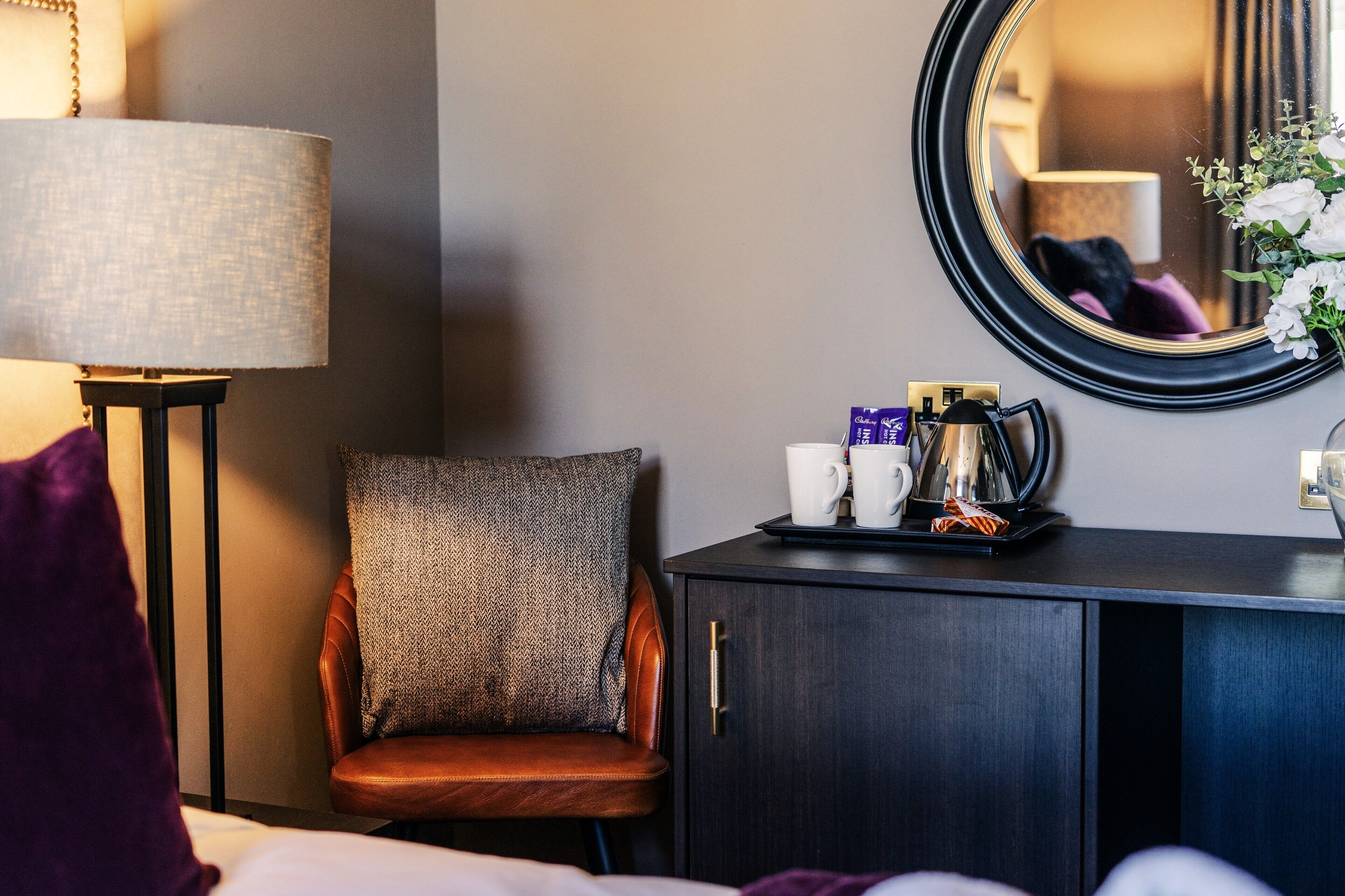 Une chambre d’hôtel avec un lit, une chaise, un bureau avec une lampe, une machine à café et un miroir.