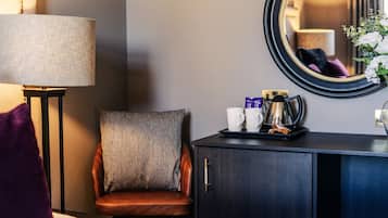 Une chambre d’hôtel avec un lit, une chaise, un bureau avec une lampe, une machine à café et un miroir.