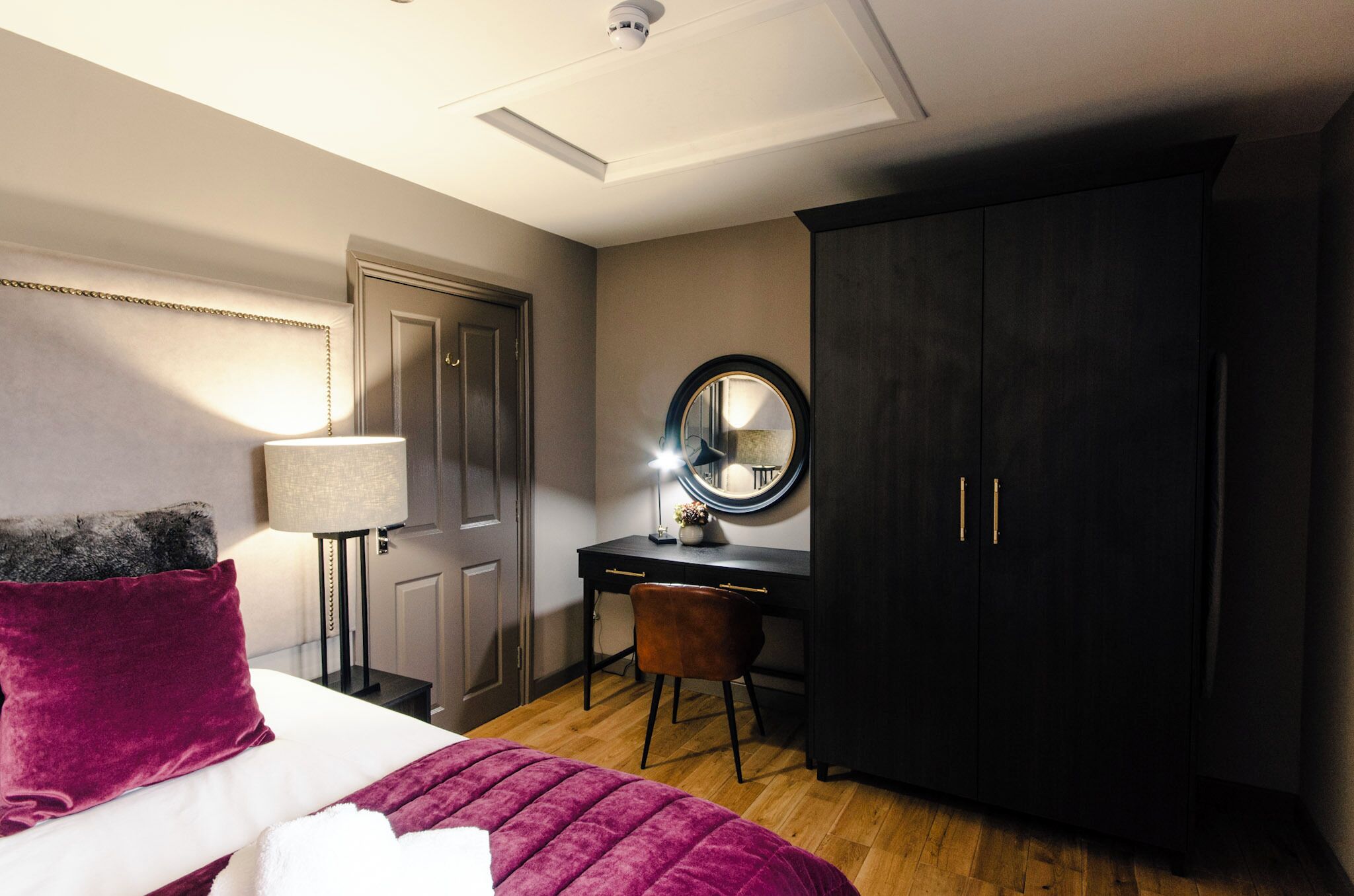 Un dormitorio con cama, escritorio, silla, armario y espejo.