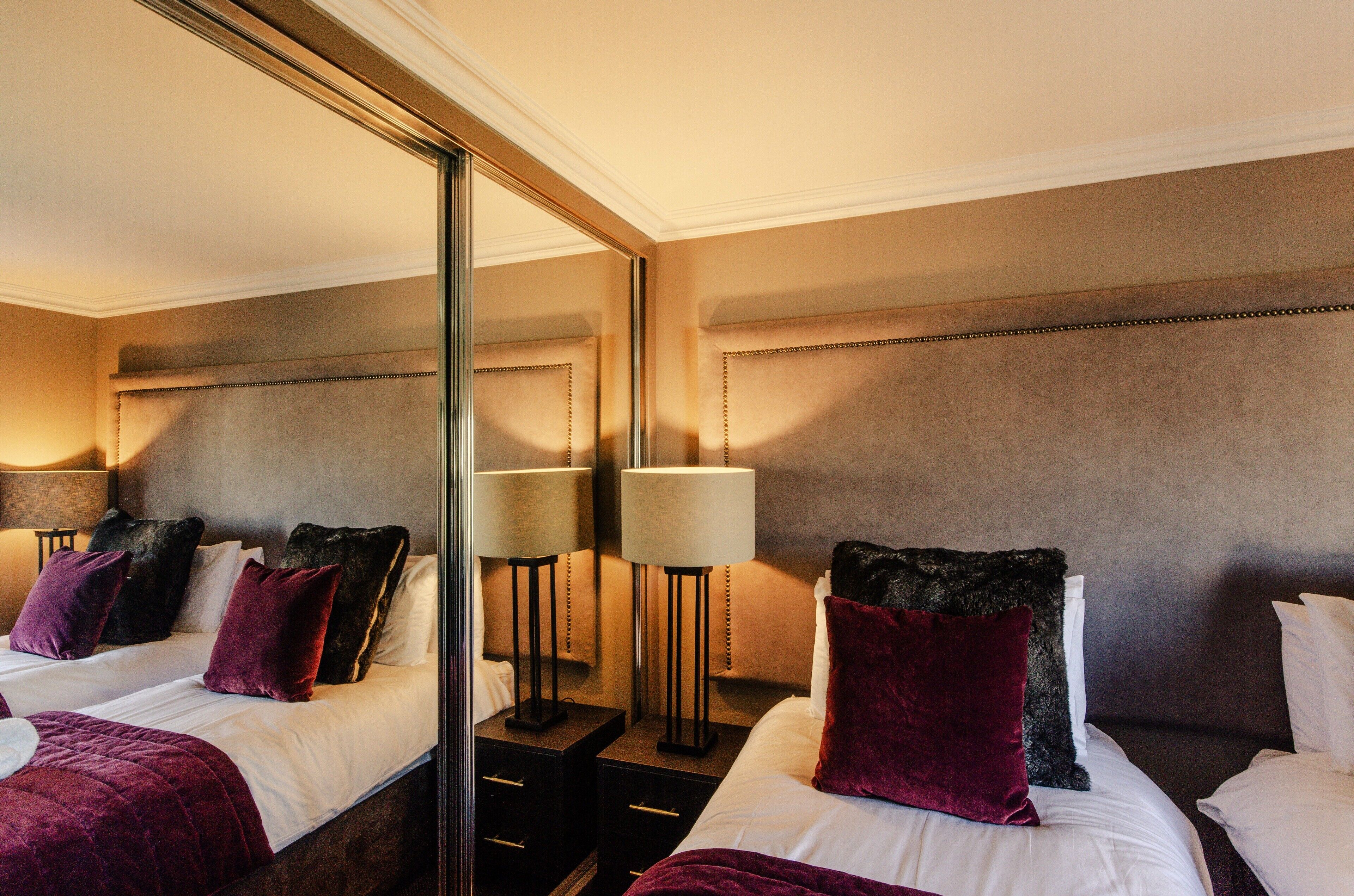 A hotel room with two beds, a large mirror, bedside lamps, and a headboard.