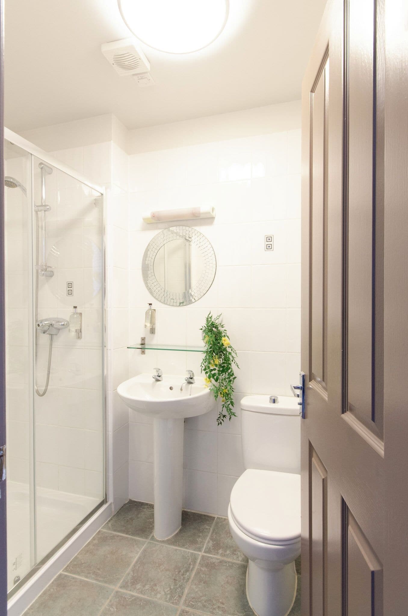 Une salle de bain avec une douche à parois de verre, un lavabo sur colonne, des toilettes et un miroir au-dessus du lavabo.
